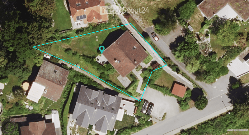 Aerial view of a residential area with multiple houses, surrounded by greenery and a road.