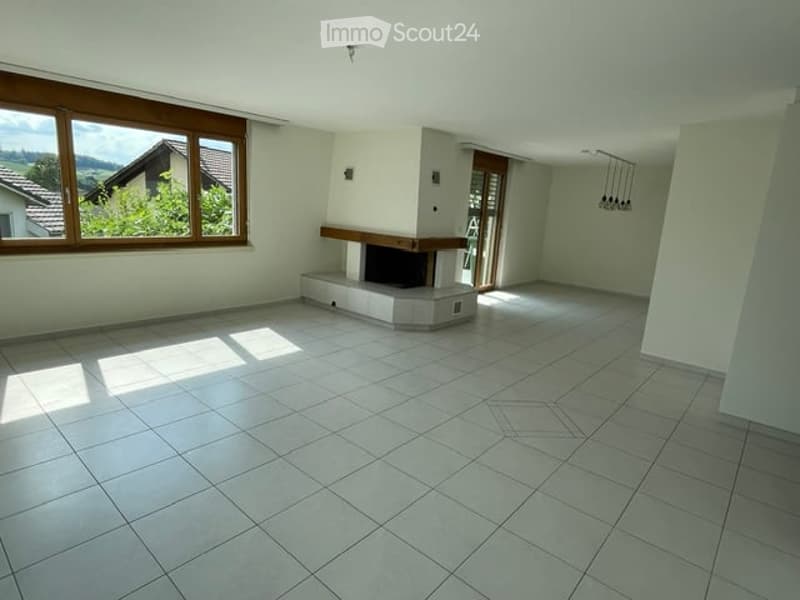 Empty living room with white tiled floor, fireplace, large windows, and sliding glass door leading to a balcony.