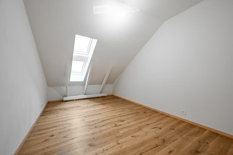 Empty attic room with wooden flooring, white walls, and skylight windows.