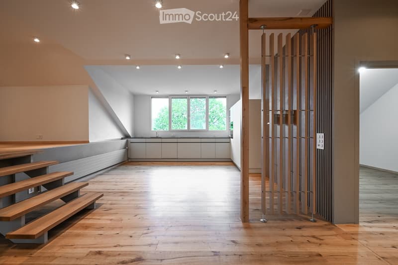 Bright, open hallway with wooden flooring, recessed lighting, and a modern wooden staircase leading to an upper level. The hallway features a sleek, minimalist design with neutral tones and large windows allowing natural light to flood the space.