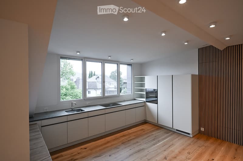 Modern kitchen with light-colored cabinets, wooden flooring, and large windows offering a view of the neighborhood.