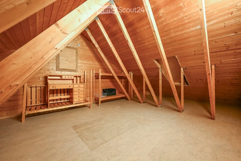 An attic space with wooden walls and ceiling beams, featuring built-in wooden shelving units and a small wooden desk area.