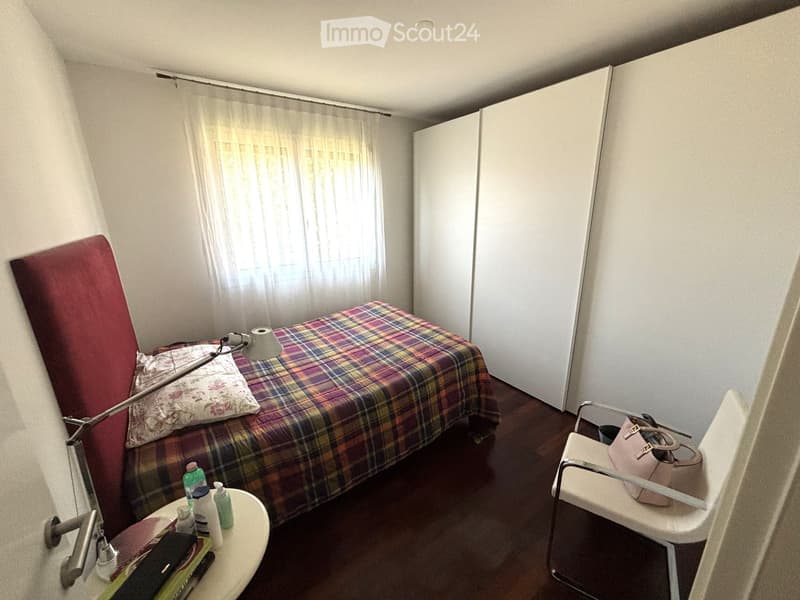 A small bedroom with a bed, a chair, a nightstand, and a window with curtains.