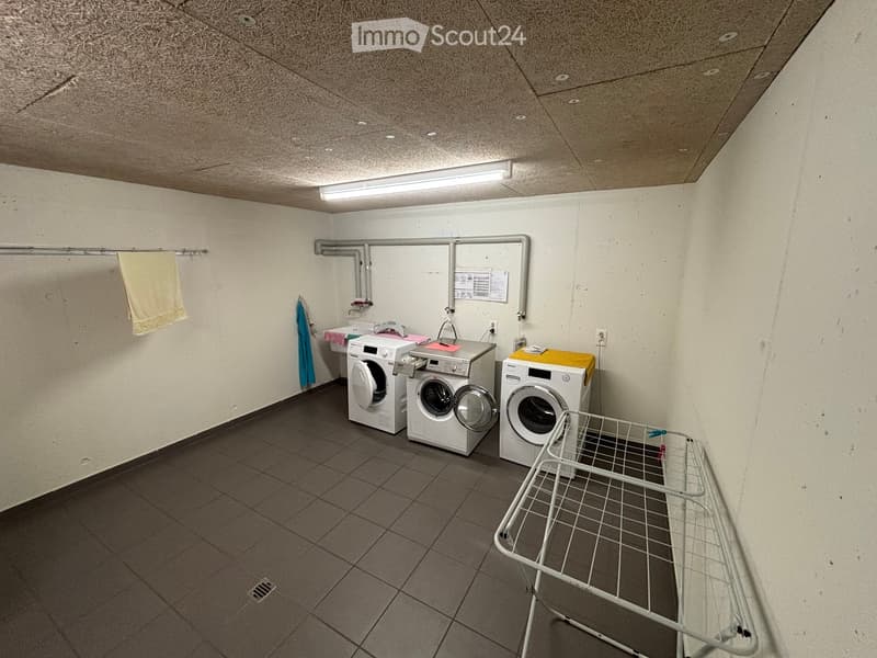two washing machines, one dryer, drying rack, tiled floor, metal pipes