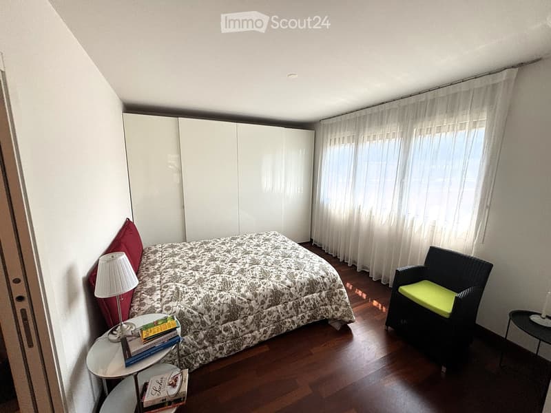 double bed, white wardrobes, wooden floors, large windows with curtains, bedside tables, armchair