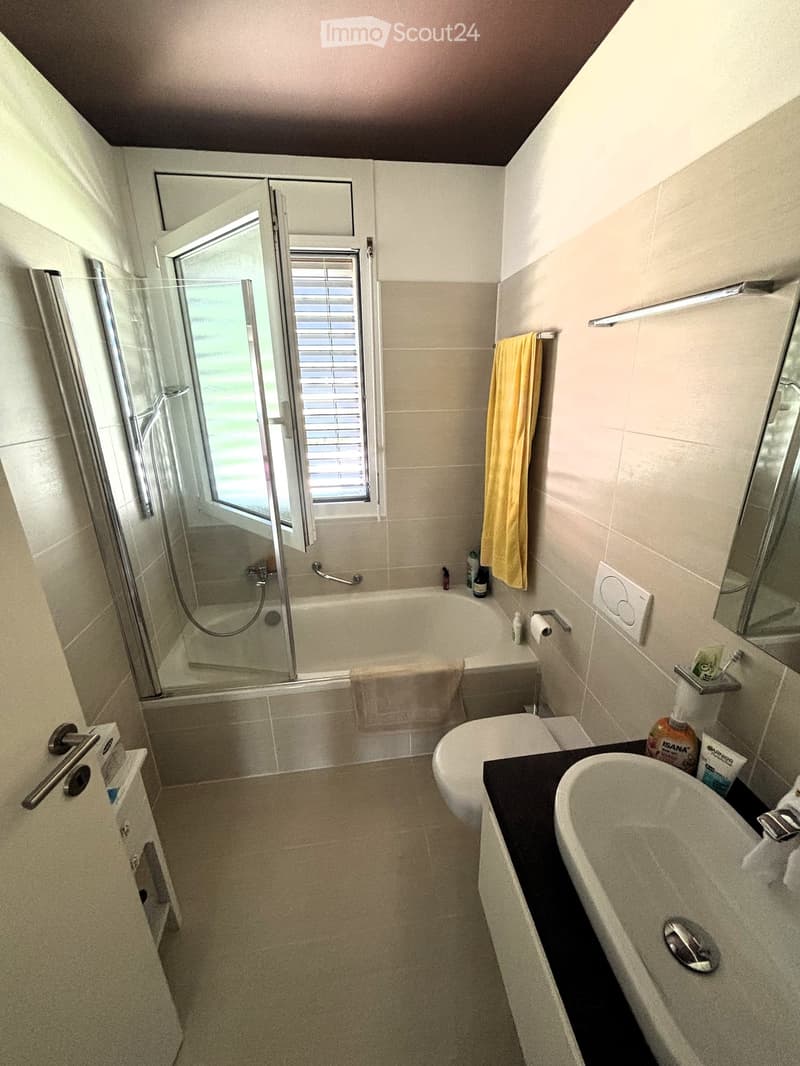 Modern bathroom with a bathtub, toilet, sink, mirror, and a glass-enclosed shower. Includes a towel, toothbrush holder, and soap dispenser.