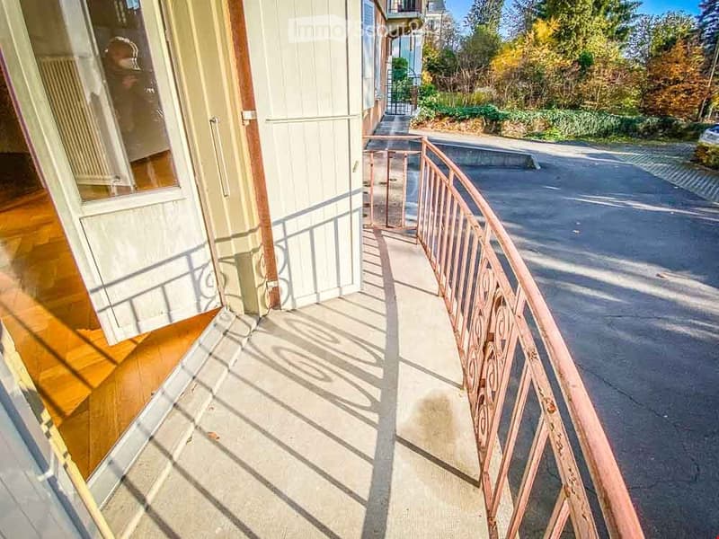Balcony with wooden floor, metal railing, and view of street and greenery.