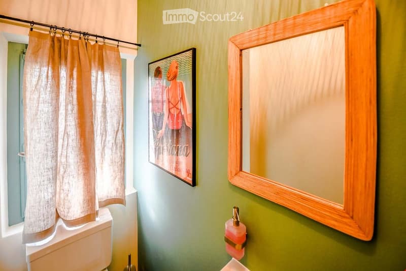 Bathroom with green walls, a wooden-framed mirror, a shower curtain, a picture frame, and a toilet.