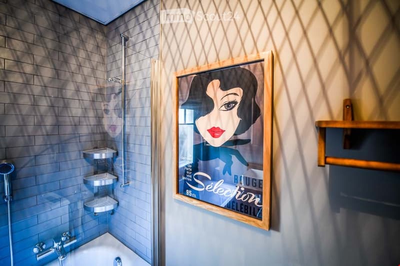 Modern bathroom with a bathtub, glass-enclosed shower, and a framed poster on the wall. The shower features a handheld sprayer and built-in shelves. A wooden shelf is mounted on the wall.