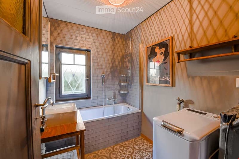 Bathroom with a sink, bathtub, and a private washing machine. Features a decorative framed picture and wooden shelves.
