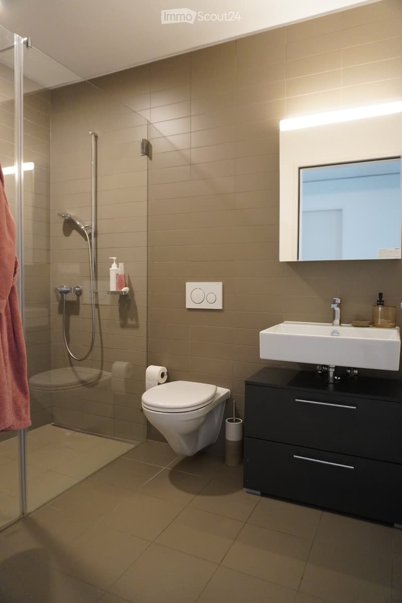 Modern bathroom with beige tiles, a glass-enclosed shower, a toilet, a sink with a mirror, and a black vanity cabinet.