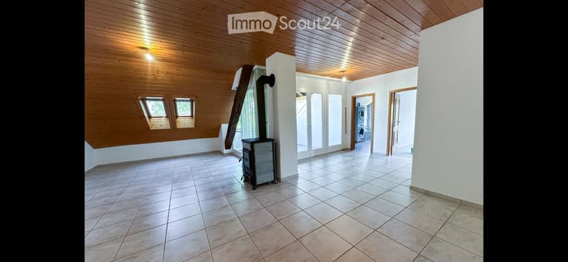Empty room with tiled floor, wooden ceiling, and a small wood-burning stove. The room has large windows and doors leading to another area.