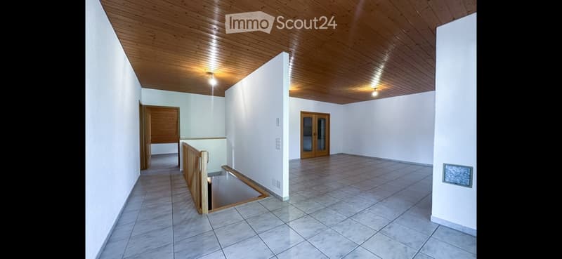 Empty room with white walls, tiled floor, wooden ceiling, and a staircase leading to another level.