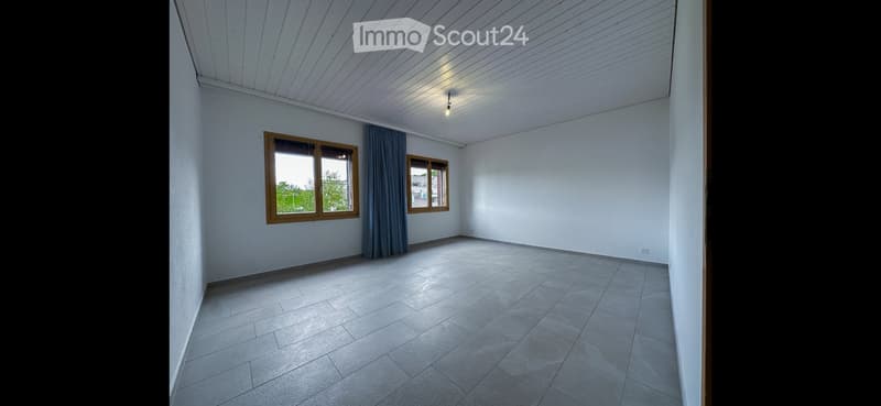 Empty room with white walls, tiled floor, and two windows with wooden frames and blue curtains.