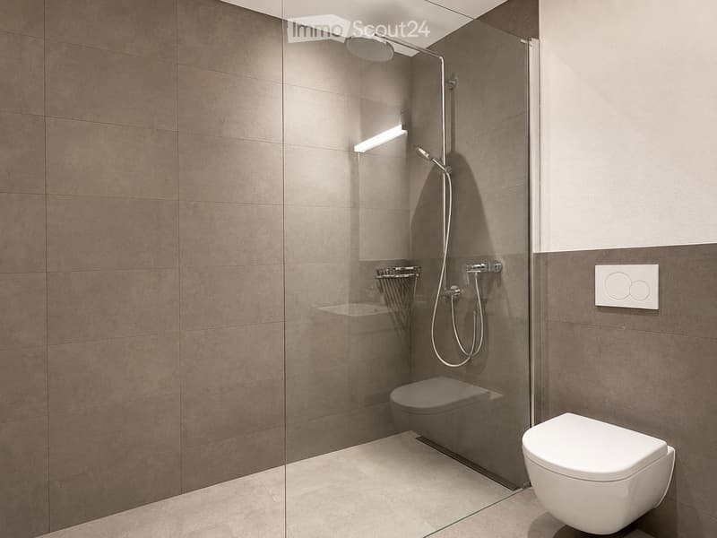 Modern bathroom with a glass-enclosed shower, a toilet, and a sleek showerhead. The walls are tiled in a warm, neutral tone, and the floor is tiled in a light beige color.
