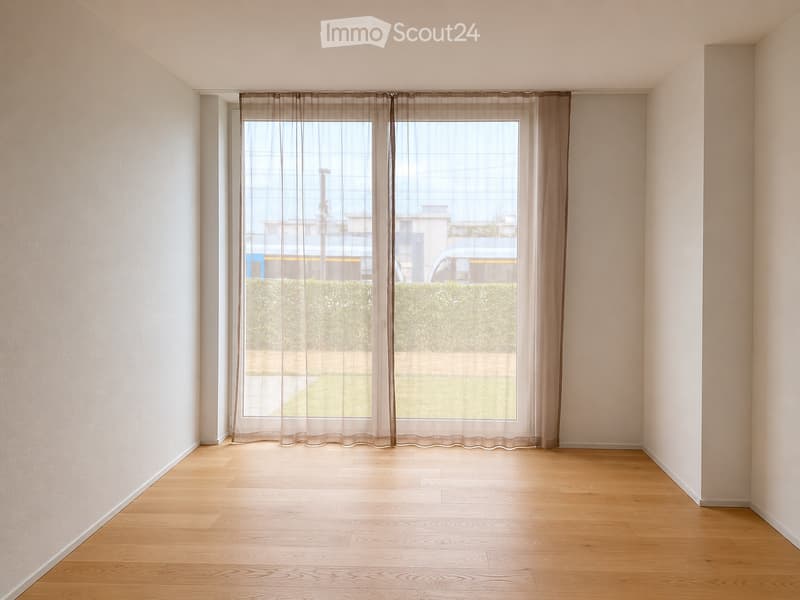 Empty room with light wooden flooring, white walls, and large window with sheer curtains. No furniture or equipment present.