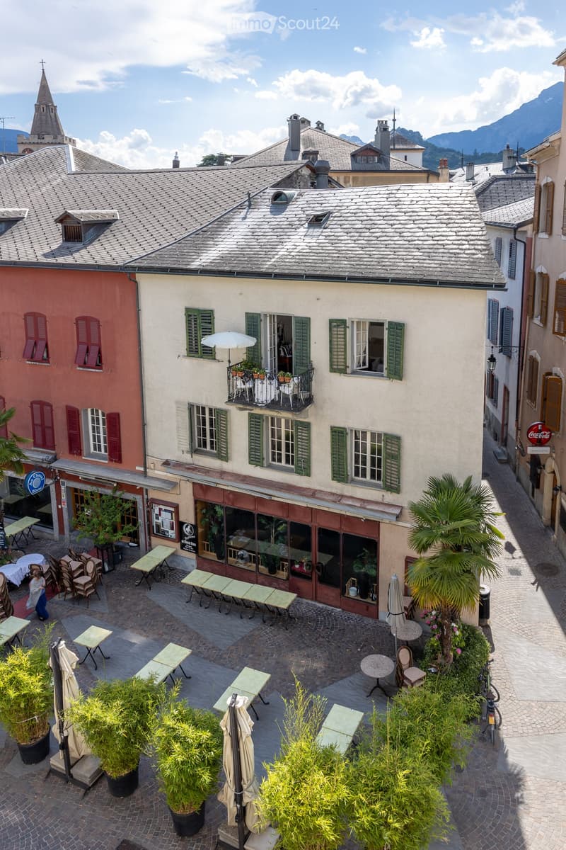 Courtyard with outdoor seating, tables, chairs, potted plants, and a small balcony with greenery and an umbrella.