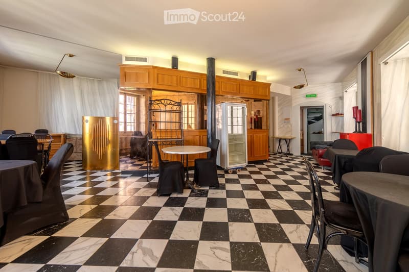 A spacious, elegantly furnished room with a black and white checkered marble floor, multiple tables and chairs, a refrigerator, wooden cabinets, and large windows with curtains.