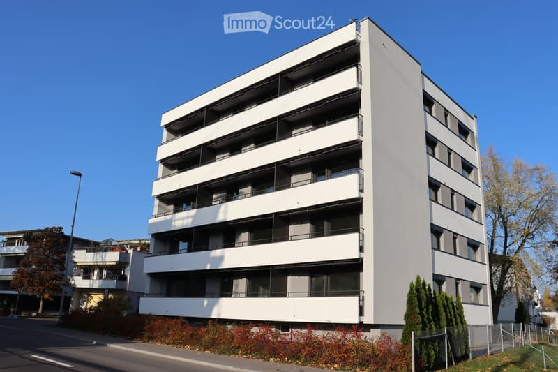 Modern multi-story apartment building with white facade, multiple balconies, and contemporary design.