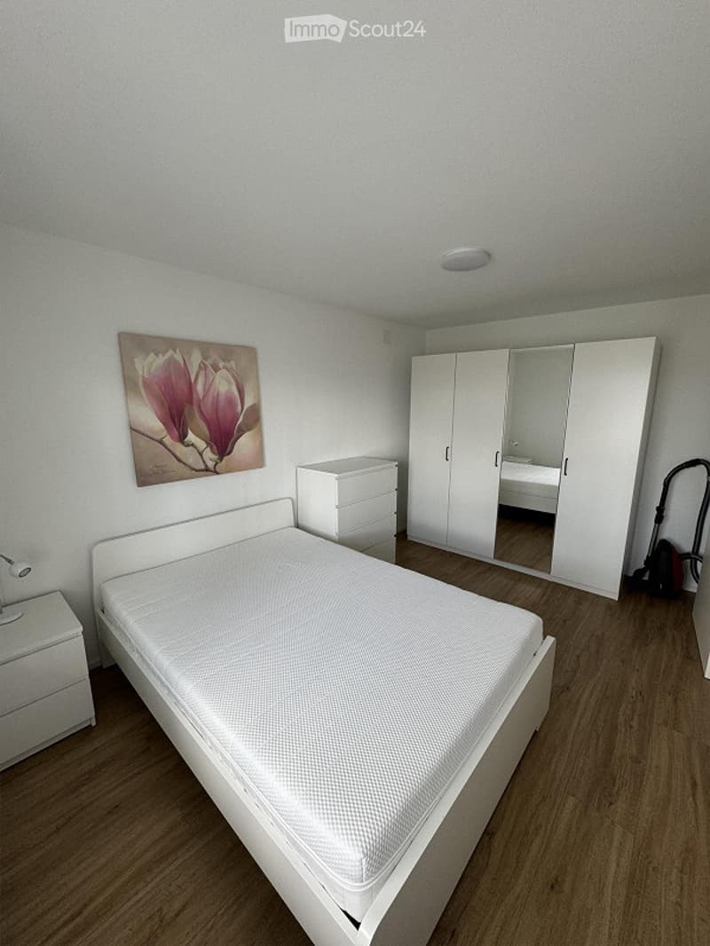 Modern bedroom with a white bed, nightstand, wardrobe with mirrored doors, and a painting of a magnolia flower on the wall.