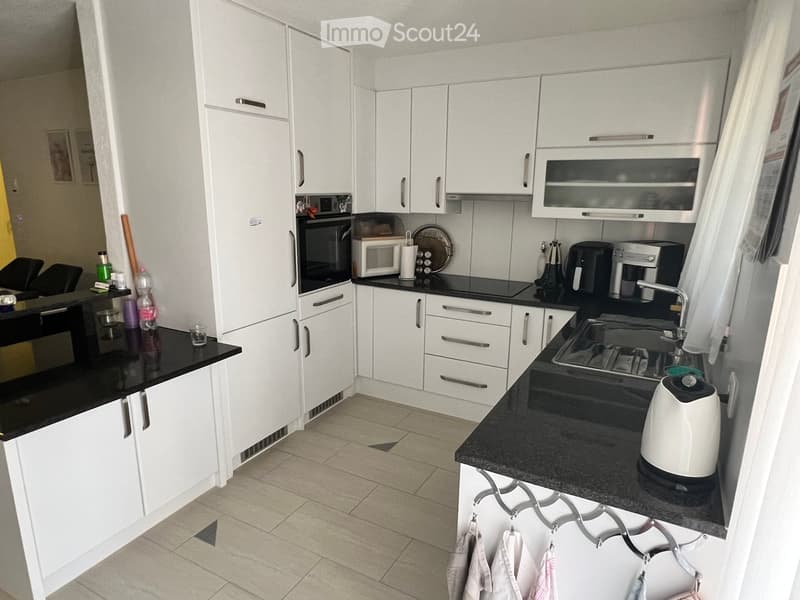 Modern kitchen with white cabinets, black countertops, and stainless steel appliances including a microwave, oven, coffee maker, and kettle. A sink with a modern faucet is visible, along with various kitchen items on the counters.