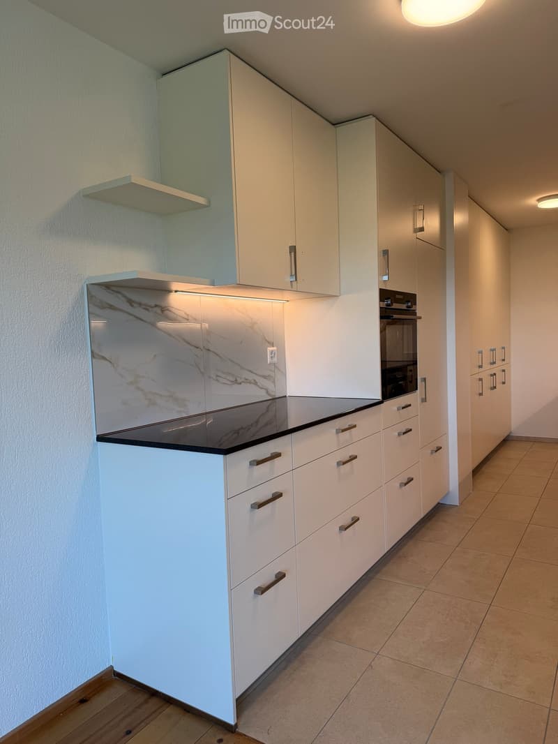 Modern kitchen with white cabinets, marble countertop, and built-in oven. Features sleek design with integrated lighting and ample storage space.
