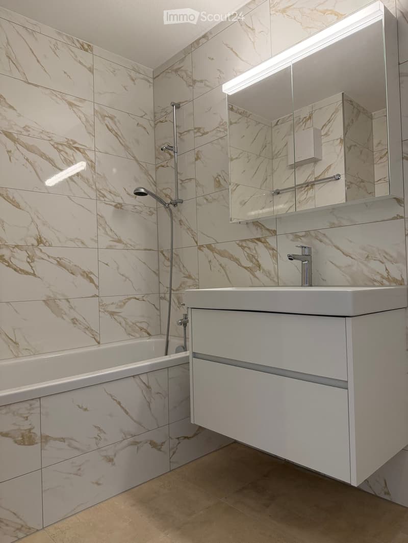 Modern bathroom with marble tiles, a bathtub, a sink with a faucet, a mirror, and a showerhead.