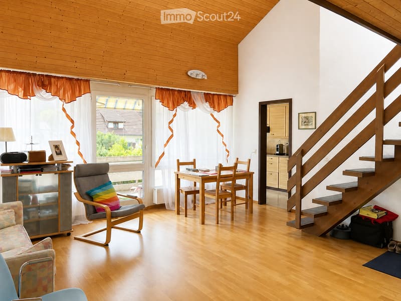 Bright living room with wooden floors, a staircase leading to another level, a sofa, a chair, a dining table with chairs, a lamp, and a view of the garden through large windows.