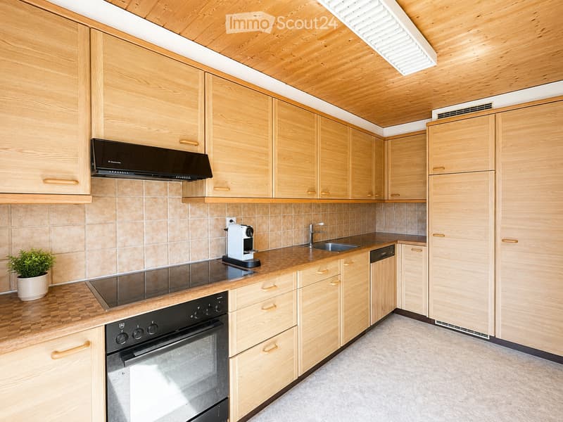 Modern kitchen with light wooden cabinets, stainless steel appliances, and a tiled backsplash.