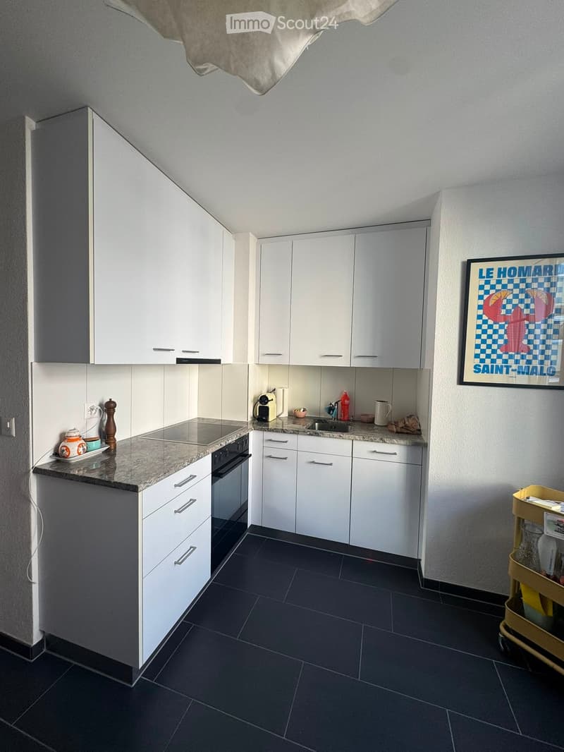 Modern kitchen with white cabinets, granite countertops, and stainless steel appliances. Includes an oven, sink, and various small items on the counter.