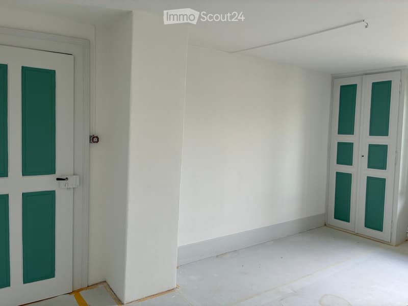 Empty room with white walls, a central column, and two green-paneled doors.