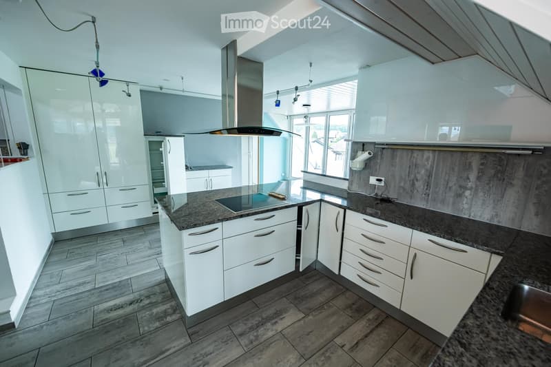 Modern kitchen with white cabinets, granite countertops, and stainless steel appliances, including a stove and range hood. The space features wooden flooring and ample natural light from large windows.