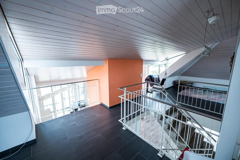 Modern interior with wooden ceiling, dark tiled floor, white railing, and furniture including a chair, table, and bed.