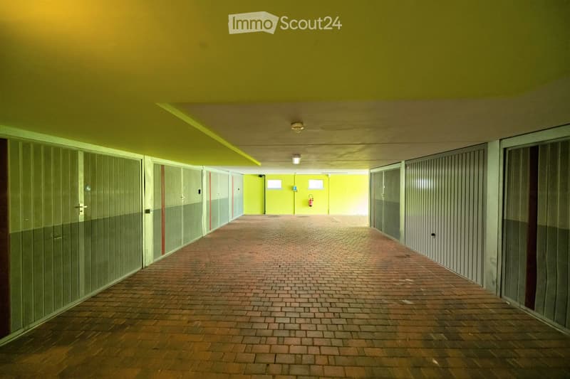 Brightly lit corridor with yellow walls, brick floor, glass-paneled doors, and a fire extinguisher mounted on the wall.