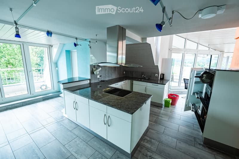 Modern kitchen with white cabinets, granite countertop, stainless steel appliances, and large windows offering a view of greenery.
