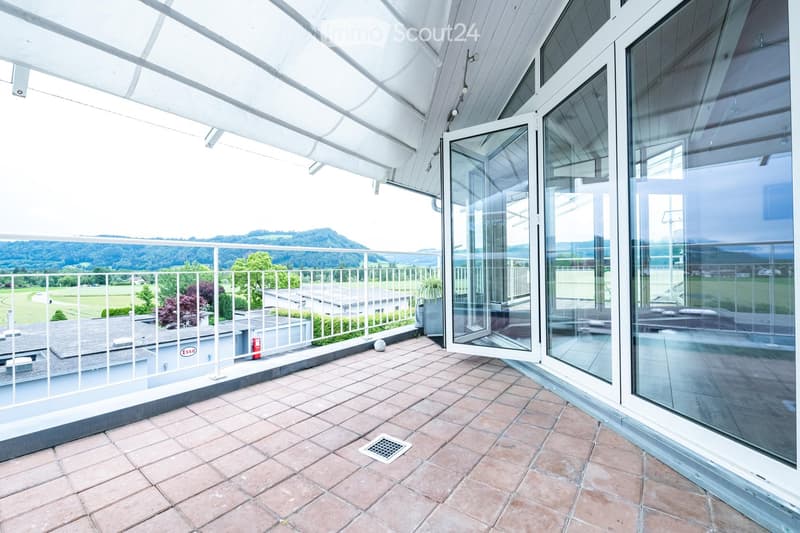 Balcony with tiled floor, white railing, large glass doors, scenic view of green landscape and mountains.