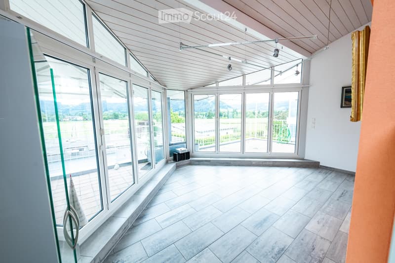 Bright, open room with large glass windows and doors leading to an outdoor area, featuring a tiled floor and white walls.
