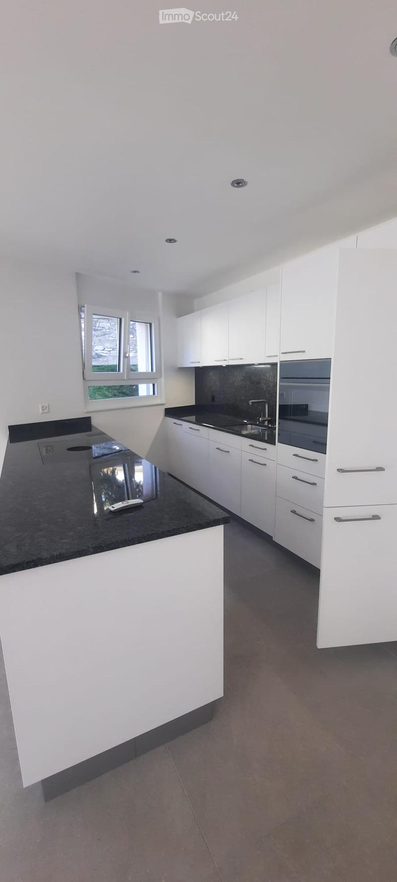 Modern kitchen with white cabinets, black countertops, and stainless steel appliances. Features a large window and a central island with a black countertop.