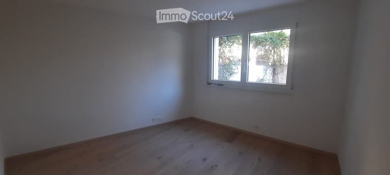 Empty room with wooden flooring and a single window showing outdoor greenery.