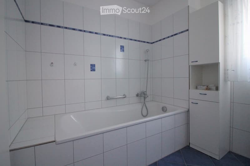 Modern bathroom with a white bathtub, tiled walls, a shower hose, and a white cabinet with a mirror.