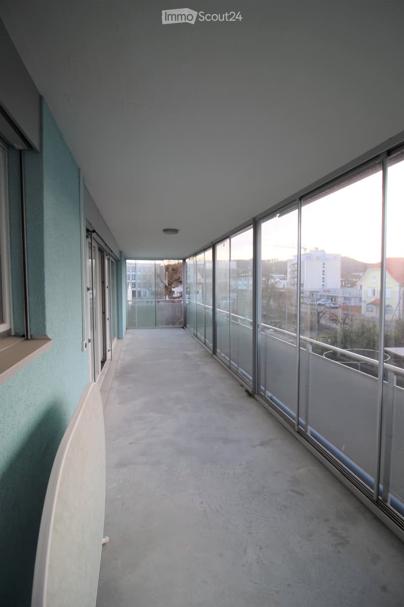Empty balcony with concrete floor, glass railings, and a view of the cityscape.