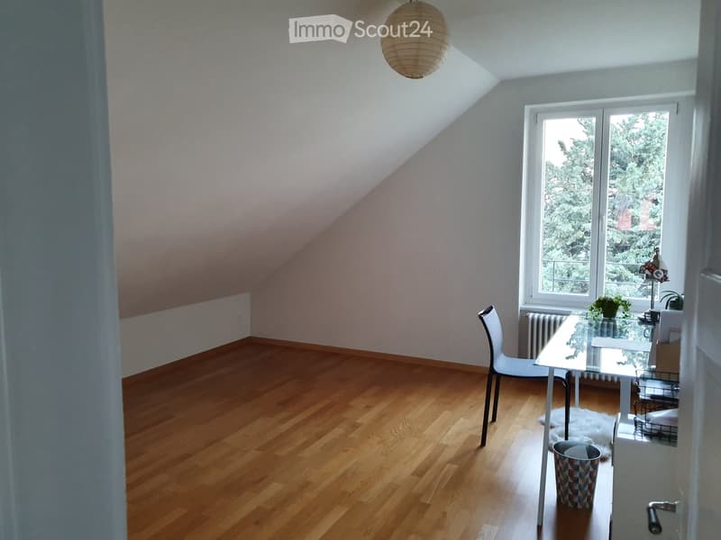 Bright, unfurnished room with wooden flooring, large window, and a single chair and table setup.