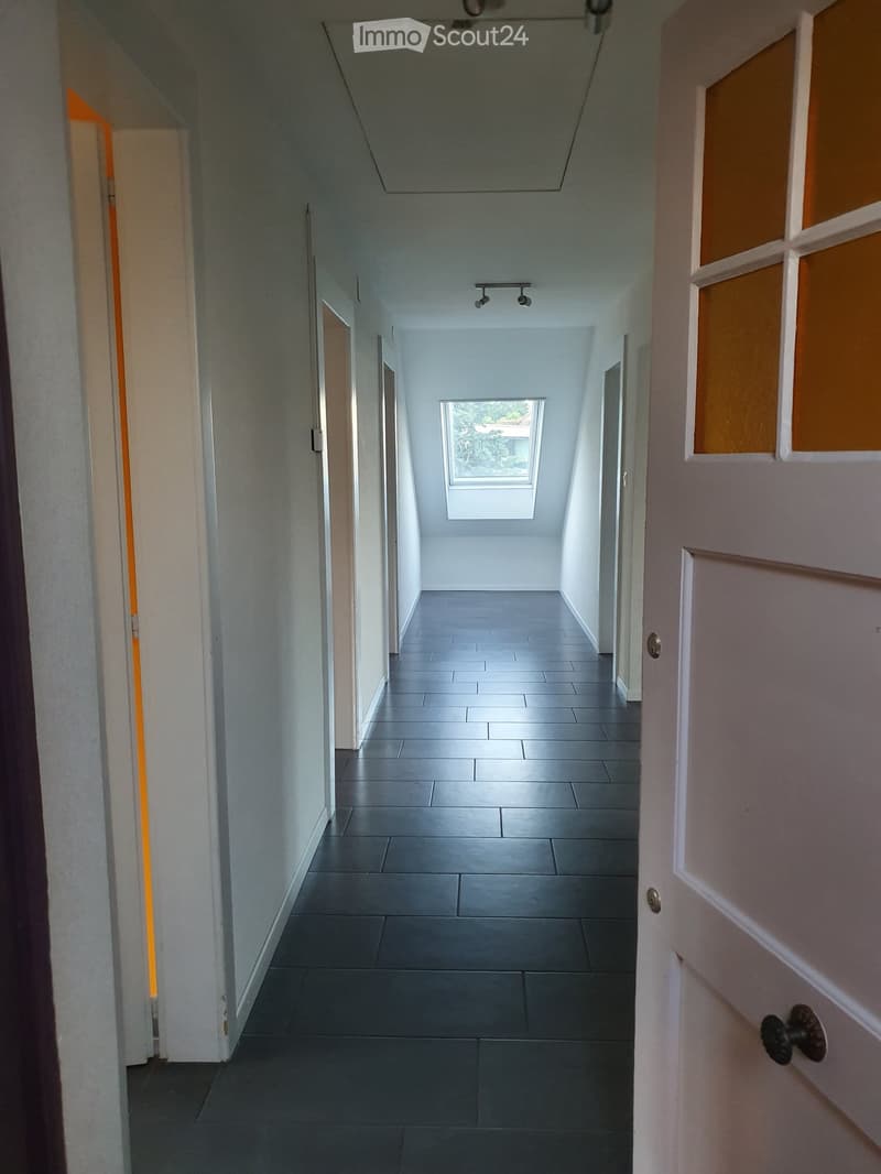 Empty hallway with grey tiled floor, white walls, and a skylight at the end. Doors are visible on both sides.