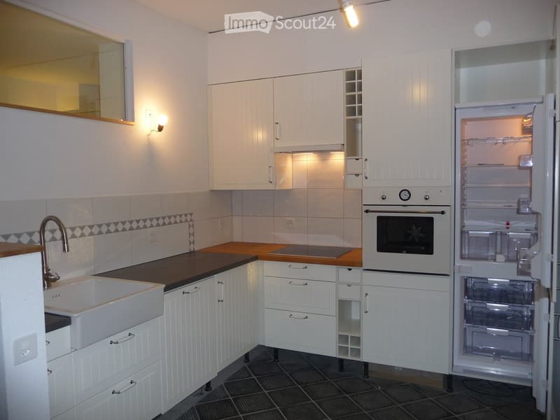 Modern kitchen with white cabinets, a sink, an oven, and an open refrigerator. Features a dark countertop and tiled backsplash.
