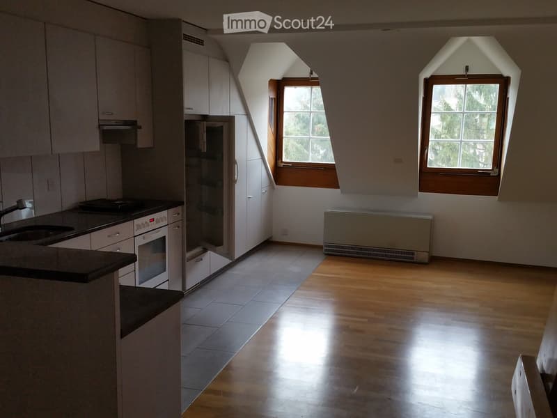 Modern kitchen with white cabinets, stainless steel appliances, and wooden flooring. Features a sink, oven, refrigerator, and ample natural light from two windows.