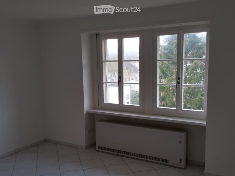 Empty room with tiled floor, white walls, large windows, radiator, and window sill.