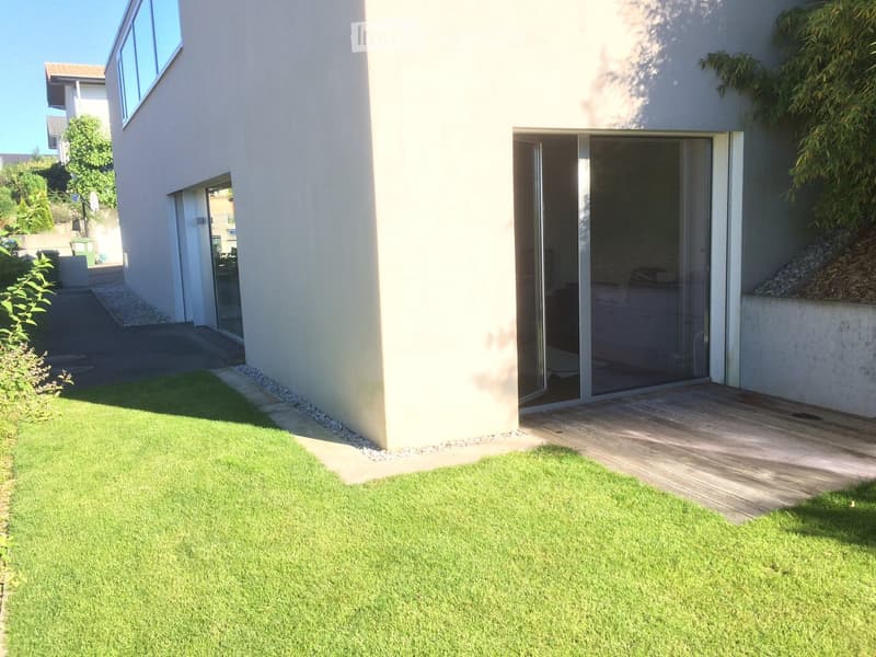 Modern house exterior with a well-maintained lawn, wooden deck, and sliding glass doors leading to the interior.