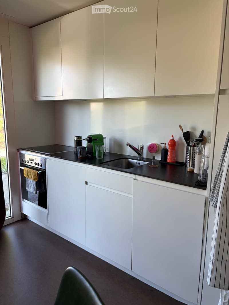 Modern kitchen with white cabinets, black countertop, stainless steel sink, and various appliances and utensils.