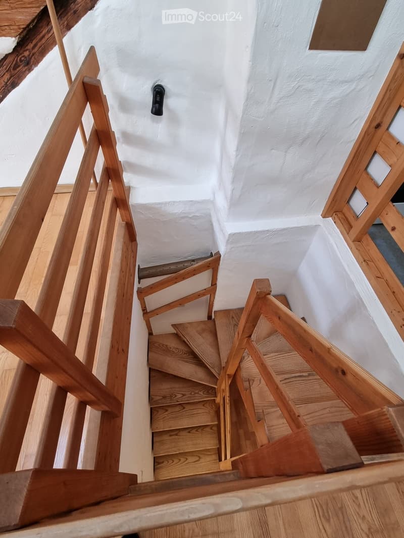 Close-up of interior wooden stairs with wooden railings and a white wall behind