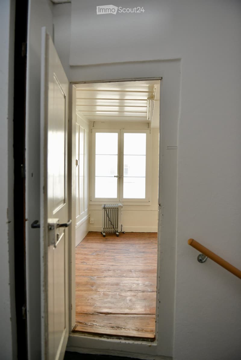 Corridor with wooden floors, white walls, double windows, radiator, and an open door